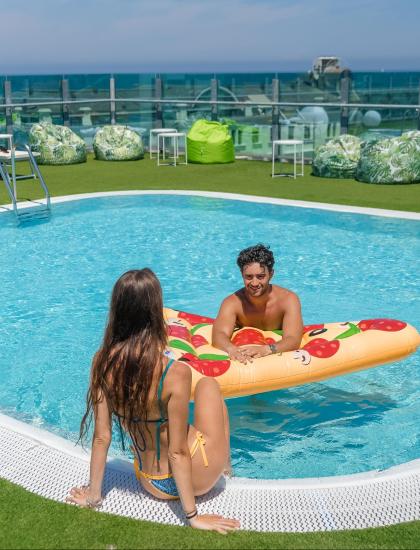 Due persone si rilassano in piscina con un materassino gonfiabile a forma di pizza.