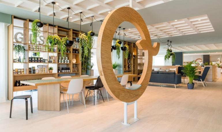 Moderno spazio lounge con tavoli, sedie e decorazioni verdi.