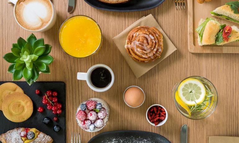 Colazione ricca con pane, croissant, pancetta e bevande.