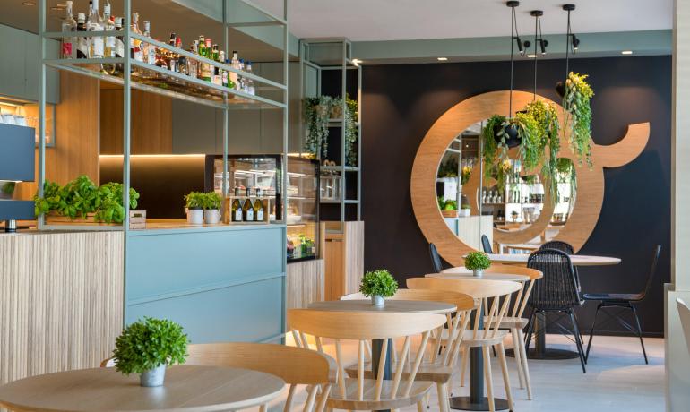 Caffetteria moderna con piante e arredi in legno chiaro.