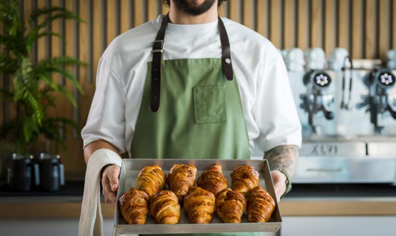 Uomo con grembiule verde tiene vassoio di croissant freschi.