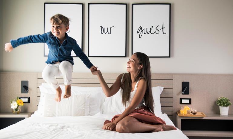 Bambino salta sul letto, donna sorride, decorazione accogliente.