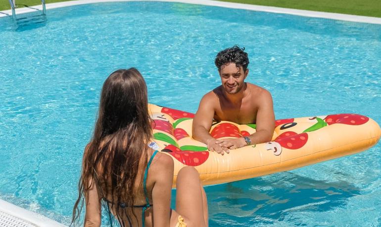Due persone si rilassano in piscina con un materassino gonfiabile a forma di pizza.